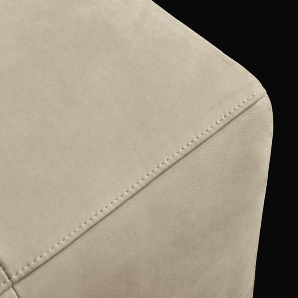 Close-up of a beige upholstered furniture corner with visible stitching against a black background.
