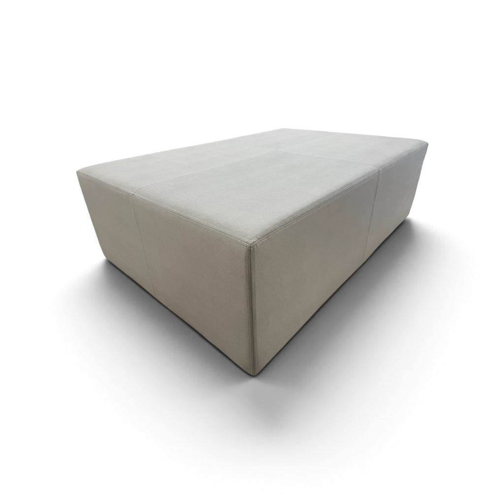 A modern rectangular upholstered ottoman or low coffee table in a light beige fabric, shown from an elevated angle on a white background.