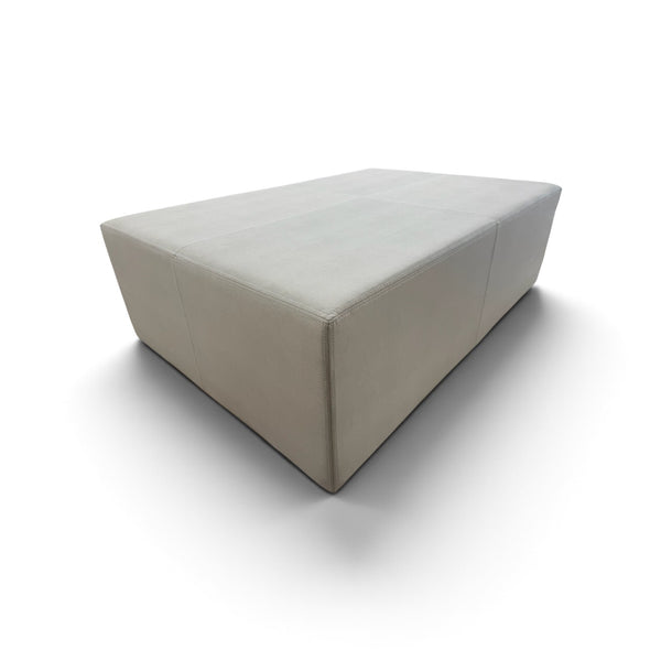 A modern rectangular upholstered ottoman or low coffee table in a light beige fabric, shown from an elevated angle on a white background.